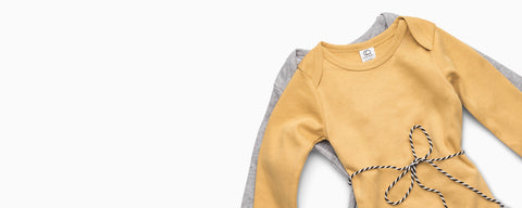 Organic cotton baby gifts under $25 including onesies, pants, and accessories laid flat on white background