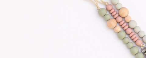 Baby pacifier clips in multiple colors attached to organic cotton clothing